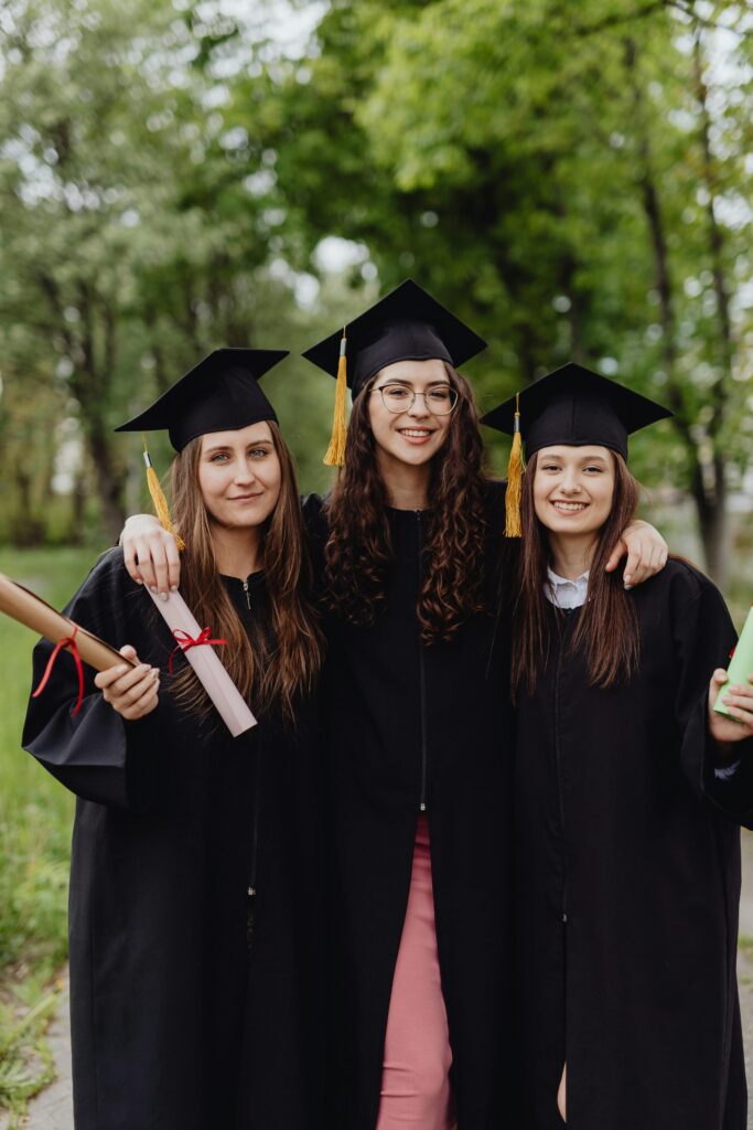 Three female graduates in caps and gowns celebrating their academic success outdoors.